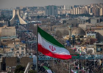 Irán se encuentra atrapado entre la dicotomía del tiempo ideológico (basado en aniversarios de la Revolución y mártires) y el tiempo material que se ha agudizado drásticamente al llegar a inicios de 2026. La "resistencia" que pregona el régimen choca con una realidad donde la supervivencia diaria es el verdadero acto de resistencia para la población. Varios factores explican por qué el sistema "aguanta" a pesar de que la brecha se ha vuelto obscena: La Economía de Guerra y el Pan: Con una inflación que no da tregua, el gobierno ha priorizado el control de suministros básicos para evitar estallidos sociales por hambre, aunque esto signifique un estancamiento total del desarrollo. La medición del tiempo en "precios del pan" es hoy la métrica de estabilidad más crítica para Teherán. La Mutación de la Represión: Tras los ciclos de protestas de años anteriores, la obediencia ya no se busca mediante el consenso revolucionario, sino a través de una vigilancia tecnológica avanzada y una presencia constante de fuerzas de seguridad en las periferias. El miedo se ha institucionalizado como el principal pegamento social. El Repliegue Geopolítico: Aunque el Estado se proclama victorioso, su "eje de resistencia" exterior ha sufrido golpes estructurales significativos entre 2024 y 2025.  Este encogimiento de la periferia militar ha obligado al régimen a concentrar sus recursos y su fuerza hacia adentro, volviéndose un sistema más introspectivo y, por ende, más asfixiante para sus propios ciudadanos. Quién manda en Irán hoy En el papel, Irán tiene presidente, gabinete, Parlamento y elecciones; en la práctica el eje es el Líder Supremo, Ali Jamenei, rodeado por un círculo de clérigos afines, viejos cuadros de la guerra Irán–Irak y mandos de la Guardia Revolucionaria. Ese núcleo decide los temas decisivos: sucesión, guerra y paz, doctrina nuclear, líneas rojas internas; el presidente gestiona el desgaste cotidiano, firma decretos y absorbe la culpa cuando la inflación se dispara o las protestas se salen de control. Desde la revuelta por Mahsa Amini en 2022, el régimen reforzó esa arquitectura: más represión preventiva, más purgas discretas en el aparato estatal, más filtros en las candidaturas y menos disidencia tolerada.​ Dentro del sistema conviven tres grupos que no se miran con confianza. El clero tradicional aporta legitimidad religiosa, controla seminarios y tribunales, pero ya no marca solo la ruta. La Guardia Revolucionaria (IRGC) monopoliza la fuerza y una porción enorme de la economía; su peso político superó hace años al del ejército regular; entre ambos se existe una capa de tecnócratas y burócratas civiles que intentan cuadrar las cuentas, negocian con China, Rusia al tiempo que intentan atraer más países a su esfera y, de paso, protegen a sus propias familias de una probable caída del sistema, cosa que nadie nombra en público.​ La Guardia Revolucionaria: cuando el país es del ejército La IRGC nació en 1979 como guardia ideológica para proteger la Revolución; cuatro décadas después parece más bien una empresa armada con bandera. Tiene sus propias fuerzas terrestres, aéreas y navales, pero el corazón del poder está en la Fuerza Quds —encargada de operaciones exteriores— y en su aparato económico: conglomerados de construcción, energía, telecomunicaciones, banca en la sombra. Su brazo de ingeniería, Khatam al-Anbia, se volvió uno de los contratistas más grandes del país, con autopistas, represas, proyectos de gas y metro adjudicados sin competencia real.​ En el tablero regional, la IRGC actúa como cancillería paralela. Maneja el programa de misiles, entrena y financia a Hezbollah en Líbano, a milicias chiíes en Irak, a grupos afines en Siria y a los hutíes en Yemen. Esa constelación, conocida como “eje de la resistencia”, le permitió a Teherán proyectar fuerza a distancia y hostigar a adversarios sin exponer directamente al Estado. Pero en 2024–2025 ese eje recibió golpes fuertes: la capacidad de Hezbollah se redujo con la ofensiva israelí, el régimen de Assad colapsó en Siria y la guerra indirecta con Israel dejó expuestas vulnerabilidades que el discurso épico no tapa.​ Economía de sanciones y vacíos Quien mire solo el PIB oficial puede pensar que Irán mantiene a flote su economía con tasas de crecimiento modestas y desempleo por debajo de 10%. Una instantánea más detallada muestra otra cosa: inflación por encima de 30% desde 2018, con picos de 40–46% en 2022–2023, que devoró ahorros y empujó a buena parte de la clase media a la pobreza. En 2024 la inflación bajó a 32,5%, pero las previsiones apuntan a un repunte por encima de 40% para 2025 y 2026; no es alivio, apenas un respiro corto.​ El rial se desplomó en el mercado libre: entre enero de 2024 y enero de 2025 perdió cerca de 62% de su valor frente al dólar, encareciendo importaciones y provocando esa sensación de que el dinero “se encoge” semana tras semana. Oficialmente, el desempleo global ronda 7–8%, pero el juvenil se mantiene en torno a 20–23%, con zonas donde analistas hablan de tasas de hasta 50–60%. La estadística no captura el subempleo ni los trabajos precarios que proliferan en las grandes ciudades: repartos, ventas informales, pequeños negocios al borde de la quiebra.​ China es el socio clave: compra petróleo con descuentos profundos, paga en yuanes y ofrece cierto colchón a cambio de contratos de largo plazo y presencia en sectores estratégicos. Rusia encontró en Irán una fuente de drones y municiones para su guerra en Ucrania; a cambio amplía cooperación militar y energética, incluido un acuerdo de seguridad anunciado en 2025. India y países de Asia Central intentan equilibrar negocios con Teherán y presiones occidentales, abriendo huecos para exportaciones de hidrocarburos y comercio regional.​ Sociedad: más allá del velo Las protestas desencadenadas por la muerte de Mahsa Amini en 2022 dejaron un surco que el régimen no logró borrar. La “nueva ley de hijab y castidad”, adoptada con fuerza en 2024–2025, endureció penas: multas desproporcionadas, vetos a servicios educativos y laborales, incluso riesgos de largas condenas de cárcel o pena de muerte para quienes desafían de forma persistente la norma.  La juventud iraní se distingue por niveles altos de educación y por una frustración igual de alta. Universidades producen ingenieros, médicos, programadores, artistas; el mercado ofrece sueldos bajos, paro persistente y la opción de emigrar si se puede. La fuga de cerebros se volvió algo común: quienes logran becas o contratos en Europa, Norteamérica o Asia generalmente no regresan, y cuando lo hacen chocan con estructuras rígidas controladas por la Guardia o por fundaciones religiosas.  Hay una pregunta que casi nadie puede responder con datos, pero se siente en los relatos: ¿cuántos iraníes creen todavía en la República Islámica como proyecto, no solo como realidad inevitable? Las encuestas independientes son escasas y riesgosas, pero testimonios de académicos, periodistas exiliados y organizaciones de derechos humanos apuntan a una erosión fuerte de legitimidad, sobre todo entre jóvenes y mujeres urbanas. La adhesión que queda se concentra en sectores beneficiados por el sistema, en parte del clero y en un segmento de población que teme el caos más que odia al régimen.​ Irán en el tablero geopolítico La relación con Israel se mueve en una guerra sin declaración. Durante años, Teherán apostó por un cerco: apoyar a Hamas en Gaza, fortalecer a Hezbollah, consolidar presencia en Siria y tejer vínculos con milicias iraquíes. El 7 de octubre de 2023 rompió inercias: el ataque de Hamas desató una respuesta que arrasó Gaza, golpeó las capacidades de Hezbollah y llevó a una escalada de choques directos entre Irán e Israel en 2025, la llamada “Guerra de los Doce Días”. Los misiles iraníes que cruzaron el cielo fueron en su mayoría interceptados.​​ Con Estados Unidos, la dinámica se congeló en una especie de “contención sin guerra”. Washington mantiene sanciones amplias, refuerza alianzas en el Golfo, persigue redes de la Guardia en terceros países; Teherán responde con sus proxies, hostigando bases, atacando buques, alimentando tensiones donde puede sin cruzar la línea que desataría un conflicto abierto, la cual estuvo a punto de desatarse en el marco de la llamada “Guerra de los Doce Días”, cuando Estados Unidos atacó instalaciones nucleares de Irán. El acuerdo nuclear de 2015 quedó sin efecto desde la retirada estadounidense en 2018, y los intentos de reanimarlo toparon con desconfianza mutua y, más recientemente, con la decisión europea de activar mecanismos para restaurar sanciones de la ONU por incumplimientos iraníes.​ Con Arabia Saudita, la historia tomó un giro distinto: en 2023 se anunció una distensión mediada por China, con reapertura de embajadas y promesas de calmar conflictos por poderes interpuestos. No borró rivalidades profundas ni conflictos en Yemen o Siria, pero redujo, al menos de forma táctica, el riesgo de choque directo; para Irán, fue una forma de mostrar que todavía puede jugar política regional más allá de las trincheras. Detrás se asoma un eje Irán–Rusia–China que muchos presentan como bloque antioccidental, aunque en la práctica está lleno de recelos: Pekín y Moscú buscan ventajas, no alianzas.​ El programa nuclear: disuasión borde Desde hace años se corea esta frase: Irán está a “semanas” de poder producir material fisible suficiente para un arma nuclear. Eso no significa que tenga una bomba ensamblada, sino que su nivel de enriquecimiento de uranio y su capacidad de centrifugado le permitirían dar el salto técnico en poco tiempo si hubiera decisión política. La comunidad internacional mira con sospecha ese umbral, más aún después de episodios de sabotaje, asesinatos de científicos y negociaciones fallidas.​ ¿Por qué Teherán no cruza la línea? El cálculo mezcla miedo y ambición. Un arma declarada podría detonar una respuesta militar, acelerar aún más sanciones y aislarlo incluso de socios que hoy le son útiles. Mantener la incertidumbre le da algo que el régimen valora: disuasión sin prueba definitiva, capacidad de usar el programa como ficha en negociaciones, herramienta para movilizar nacionalismo interno frente a presiones externas. El expediente nuclear sirve adentro como símbolo de orgullo y resistencia; afuera funciona como aviso y como moneda de cambio.​ Entra el heredero del shah en escena El hackeo a la televisión estatal iraní que permitió la emisión de un mensaje de Reza Pahlavi, hijo del último sha, se ha convertido en un episodio significativo dentro de la disputa por el control del relato político en Irán. Más allá del componente técnico, el incidente ilustra la fragilidad del monopolio informativo del Estado, la evolución de las tácticas opositoras y el grado de polarización en torno a la figura de la monarquía exiliada y a la continuidad de la República Islámica. El incidente: una irrupción breve pero simbólica Según los reportes disponibles, varios canales de la radiodifusora pública IRIB son las siglas en inglés de la Radiodifusión de la República Islámica de Irán (Islamic Republic of Iran Broadcasting), vieron temporalmente interrumpida su programación cuando la señal satelital fue sustituida por un video de Reza Pahlavi, ex príncipe heredero que vive en el exilio desde la revolución de 1979. Durante unos minutos, la audiencia que esperaba contenidos habituales de la televisión estatal se encontró con imágenes del opositor hablando directamente al público iraní y a las fuerzas de seguridad, en un momento de alta tensión social. La cadena reconoció posteriormente el incidente, describiéndolo como un hackeo puntual ya resuelto, en un intento de minimizar su alcance y proyectar control sobre la infraestructura de medios. Aunque la duración exacta de la transmisión intervenida varía según las crónicas, el consenso es que fue breve, lo suficiente, sin embargo, para que numerosos usuarios grabaran y redistribuyeran el contenido en redes sociales y aplicaciones de mensajería. Esta circulación secundaria amplificó el impacto del jacking mucho más allá del tiempo estrictamente “robado” a la señal de IRIB.  La televisión estatal constituye una de las principales herramientas de legitimación del régimen. No solo ofrece la versión oficial de los hechos, sino que también se utiliza para presentar a la oposición como marginal, desorganizada o manipulada desde el exterior. La irrupción de Pahlavi en esa misma pantalla subvierte temporalmente esa lógica: el opositor aparece en “casa ajena”, en el espacio más controlado por el sistema, y lo hace sin mediación oficial. El episodio, aunque breve, funciona como un recordatorio de que ningún dispositivo de propaganda es completamente invulnerable en un entorno digitalizado e interconectado. Escenarios para los próximos años El régimen mantiene cohesión en la cúpula, evita fracturas abiertas en la Guardia, distribuye lo justo de renta petrolera y represión para impedir explosiones masivas.  La inflación vuelve al rango de 40–45%, el rial sigue cayendo, la inversión se seca y el desempleo juvenil se dispara por encima de los niveles ya preocupantes. El Estado responde con más control, pero pierde capacidad de ofrecer servicios básicos y subsidios.  Ante una crisis sucesoria o una nueva ola de protestas, la Guardia decide dejar de gobernar desde las sombras y toma espacios formales, quizá con un presidente salido de sus filas. La fachada religiosa se mantiene, pero el peso de los clérigos en decisiones clave se reduce. Un sector del establishment —tecnócratas, parte del clero, figuras pragmáticas de la Guardia— impulsa ajustes para evitar estallidos mayores: cierta apertura en política económica, diálogo limitado con Occidente, relajación parcial en normas sociales urbanas.  Una escalada con Israel —derivada de una acción de Hezbollah, un ataque contra instalaciones nucleares o un incidente en Siria— podría desencadenar una confrontación directa acotada. Irán buscaría evitar una guerra total, pero aun un choque “limitado” dañaría infraestructura, aceleraría la crisis económica y abriría oportunidades y riesgos internos para quienes sueñan con cambiar el rumbo.​​
